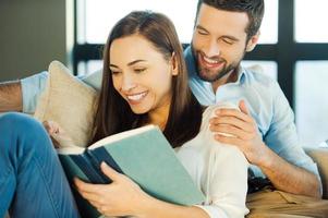 Enjoying every moment together. Beautiful young loving couple bonding to each other and smiling while woman reading a book photo