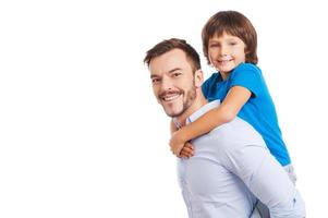 padre e hijo. vista lateral del padre feliz cargando a su hijo en la espalda y sonriendo mientras ambos están aislados en blanco foto