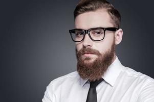 retrato de confianza y creatividad. apuesto joven barbudo con camisa y corbata mirando a la cámara mientras se enfrenta a un fondo gris foto