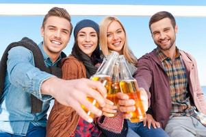 anima a un grupo de jóvenes felices animando con cerveza y sonriendo mientras se unen entre sí foto