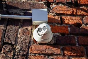 Spherical white video camera mounted on an old red brick wall in sun photo