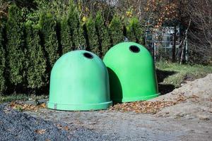 Two green spherical garbage containers standing on pathway with gravel and sand in front of fir trees photo