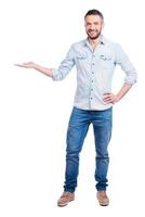 Copy space on his hand. Full length of handsome young man in casual wear holding copy space and smiling while standing isolated on white background photo