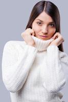 Elegance in white. Beautiful young women covering face with turtleneck while standing against grey background photo