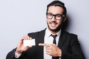 Just all this number Handsome young man in formalwear stretching out a business card while standing against grey background photo