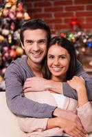 Enjoying Christmas together. Beautiful young loving couple bonding to each other and smiling with Christmas Tree in the background photo