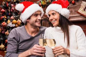 Cheers Happy young loving couple in Santa hats bonding to each other and cheering with wine and with Christmas Tree in the background photo