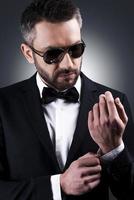 Everything should be perfect. Handsome mature man in sunglasses and formalwear adjusting his sleeve while standing against grey background photo