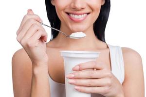 My special breakfast. Close-up of young smiling woman holding a spoon with sour cream while standing against white background photo