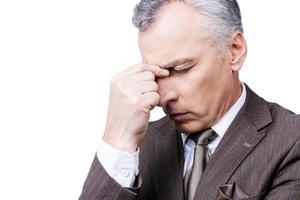 Too much problems. Frustrated mature man in formalwear touching head with fingers and keeping eyes closed while standing against white background photo