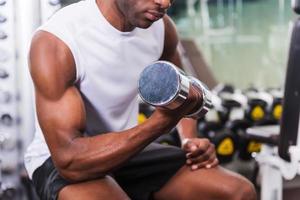 Bodybuilding. Cropped image of young African man training with dumbbell in gym