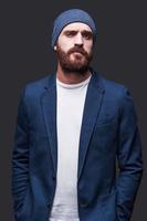 Confident and handsome. Handsome young bearded man in smart casual wear looking at camera while standing against grey background photo