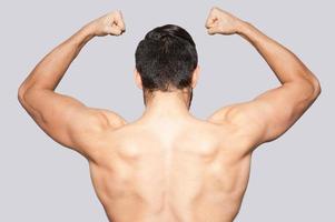 Showing his perfect body. Rear view of young muscular man posing while standing against grey background photo