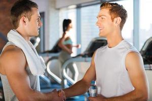 Meeting good friends in gym. Two handsome young men shaking hands and smiling while standing in photo