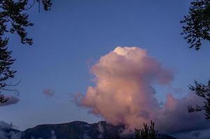 gran nube con un tinte rosa sobre un fondo de cielo azul y montañas foto