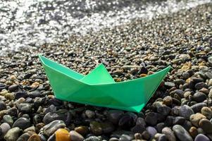 playa de guijarros de barco de papel verde en el fondo del mar. juguete hecho a mano foto