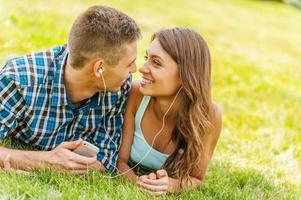 On one musical wave.  Young couple lying on the grass and listening to music together photo