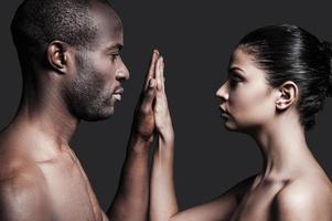 One touch and one love. Portrait of shirtless African man and Caucasian woman holding their hands clasped and looking at camera while standing against grey background photo