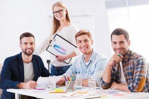 Creative team. Four cheerful business people in smart casual wear sitting together at the table and looking at camera photo