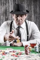 Playing poker. Serious senior man in shirt and suspenders throwing his gambling chips at the poker table photo