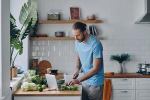 Handsome young man preparing food while standing at the kitchen counter at home photo