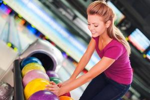 Choosing a ball. Cheerful young women choosing bowling ball and smiling while standing against bowling alleys photo