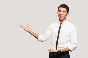 Positive selling. Confident young Afro-American man in shirt looking at camera and pointing away while standing against grey background photo