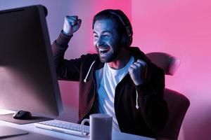 Happy young man looking at the computer monitor and gesturing against colorful background photo