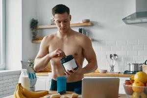 Confident fit man preparing protein drink while standing at the kitchen photo