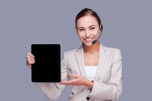 Copy space on her tablet. Confident young female operator holding digital tablet while standing against grey background photo