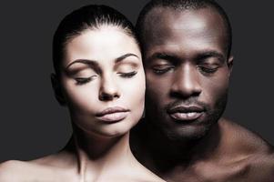 cara a cara. retrato de un hombre africano sin camisa y una mujer caucásica uniendo sus caras entre sí y manteniendo los ojos cerrados mientras están de pie contra un fondo gris foto