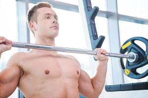 Man weightlifting. Concentrated young muscular man working out on bench press photo