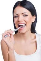 Teeth care. Portrait of beautiful young woman holding a toothbrush in her mouth and looking at camera while standing against white background photo