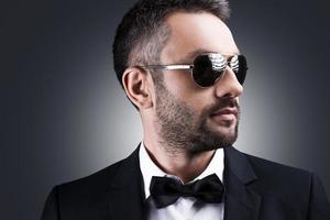 Classy and handsome. Portrait of handsome mature man in formalwear and sunglasses looking away while standing against grey background photo