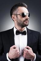 Looking just perfect. Portrait of handsome mature man in formalwear and sunglasses looking away while standing against grey background photo