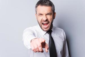 It is your fault Furious mature man in shirt and tie shouting and pointing you while standing against grey background photo