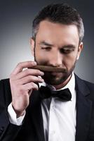 My favorite cigar. Portrait of handsome mature man in formalwear smelling cigar while standing against grey background photo