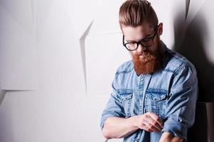 Being attentive the small details. Handsome young bearded man wearing glasses and rolling up sleeves photo