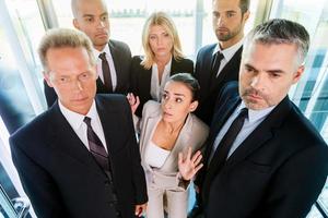 Drowning in people. Top view of fearful young woman in formalwear feeling trapped by the crowd while standing in elevator photo