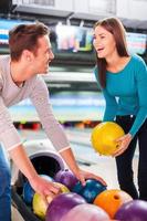 Cheerful friends. Cheerful young couple looking at each other and choosing bowling balls while standing against bowling alleys photo