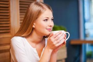 hermosa soñadora. vista lateral de una joven pensativa disfrutando de un café en la cafetería foto