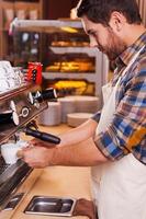 Making fresh coffee. Side view of confident barista making coffee while standing at the bar counter near the coffee machine photo