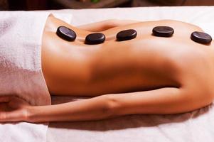 Stone SPA. Top view of young woman with shiny skin lying on front with spa stones on her back photo