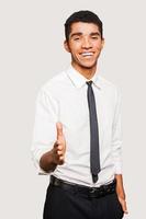 Portrait of cheerful young Afro-American man in formalwear stretching out hand for shaking while standing against grey background photo