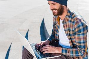 trabajo agradable al aire libre. apuesto joven barbudo sonriendo mientras trabaja en la computadora portátil foto