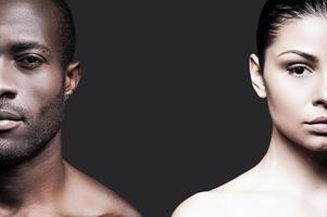 Black and white. Half faces of shirtless African man and Caucasian woman looking at camera while standing against grey background photo