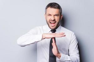 Time out Furious mature man in shirt and tie shouting and gesturing time out while standing against grey background photo