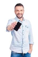 mostrando su nuevo teléfono inteligente. un joven apuesto con ropa informal que muestra su teléfono inteligente y sonríe mientras está aislado de fondo blanco foto