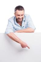 Look at that Happy young man in casual wear leaning at copy space and pointing it while standing against white background photo