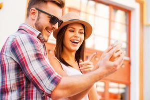 mira esta foto feliz joven pareja amorosa de pie al aire libre juntos y mirando el teléfono móvil